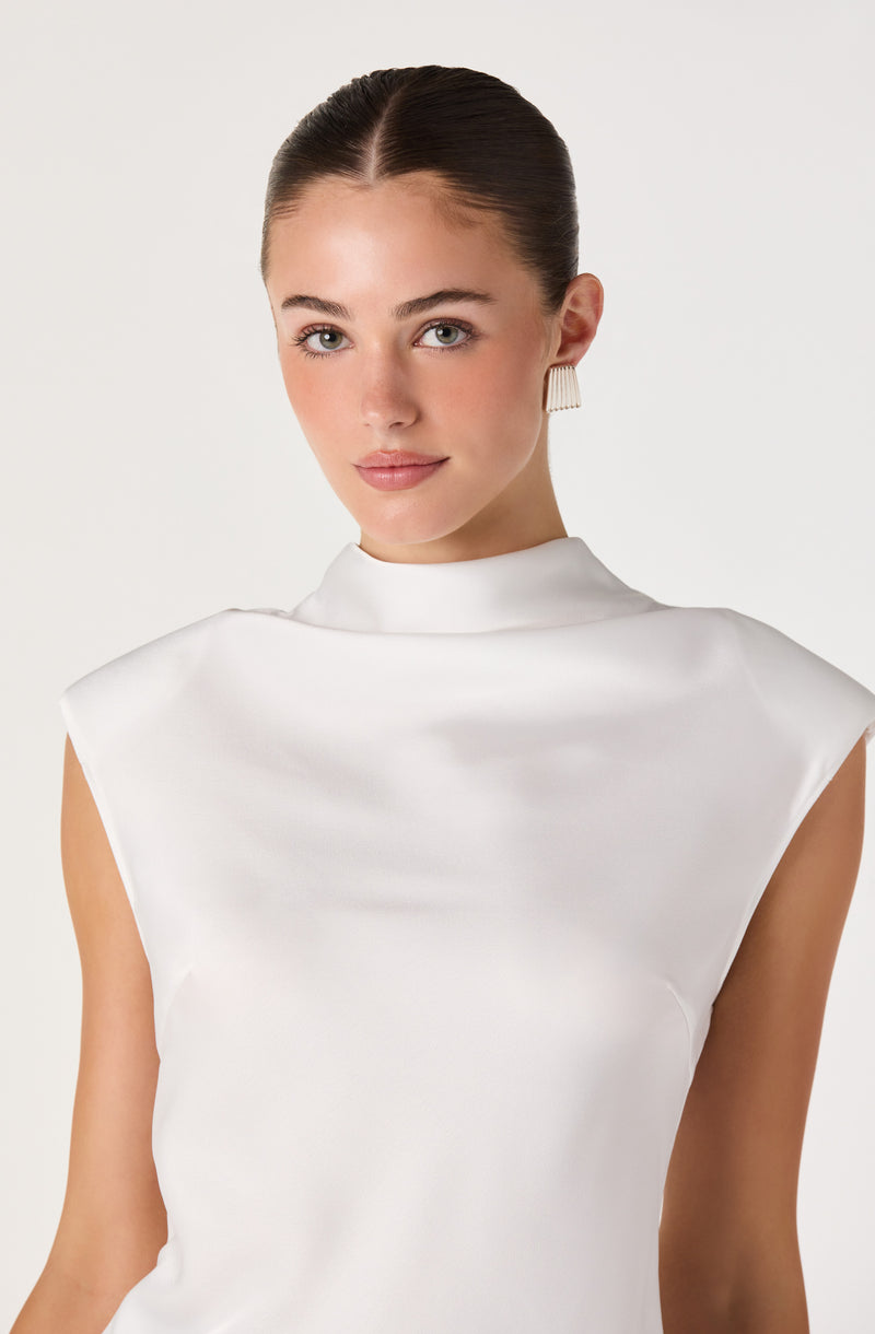 Woman wearing a sleeveless white satin top with a high collar and pleated earrings.