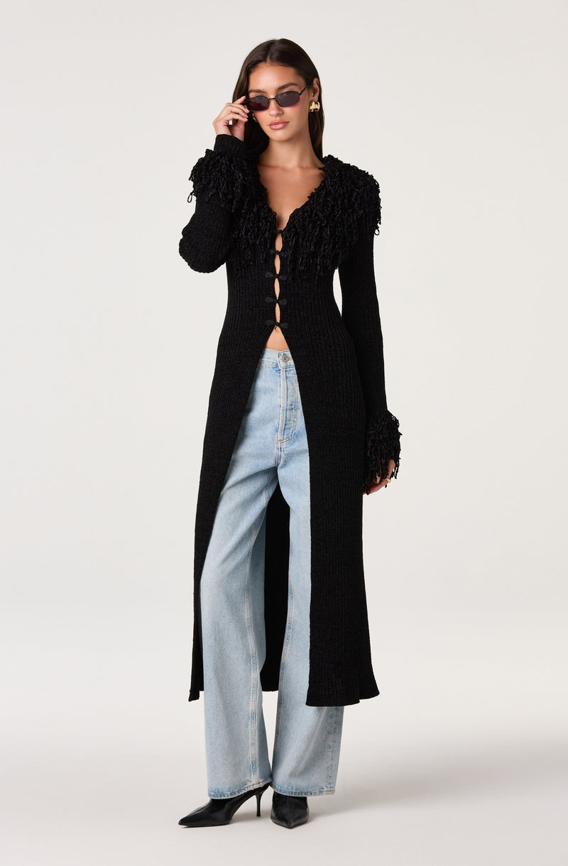 Woman wearing a long black textured cardigan with open front and wide-leg light blue jeans.