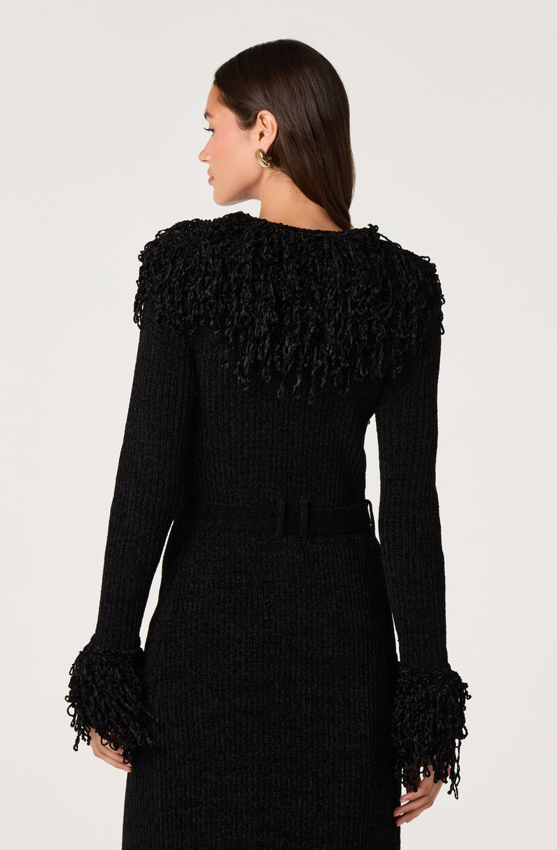 Woman in a black textured knit dress with fringed details on the shoulders and cuffs.