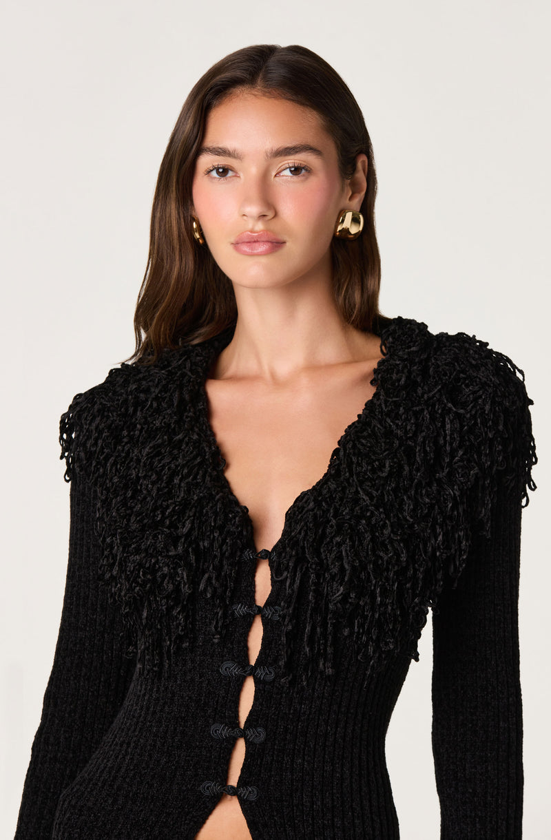 Woman wearing a black sweater with textured, ruffled shoulders and knotted front detailing.
