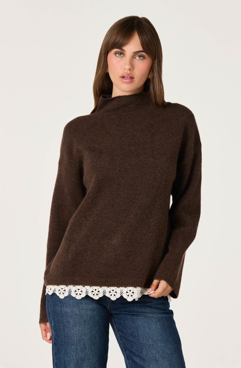 Woman wearing a brown high-neck sweater with a white lace trim at the hem, paired with blue jeans.