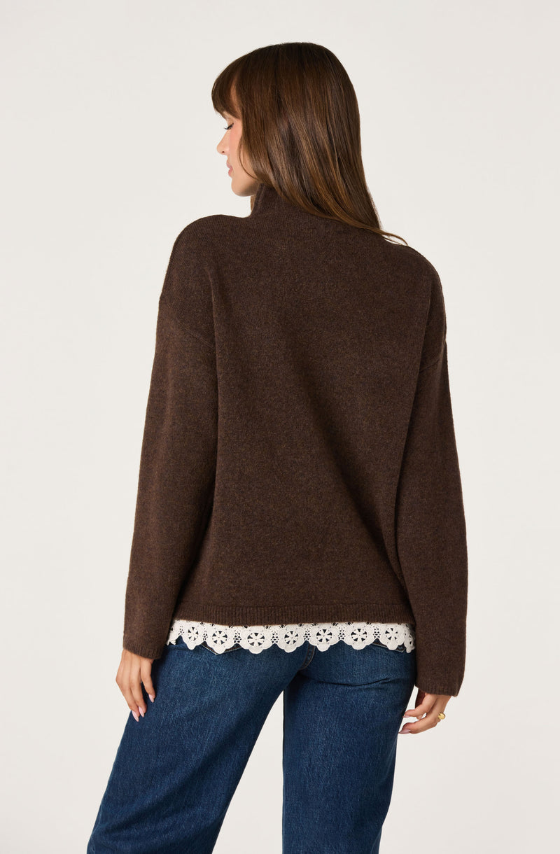 Woman in a brown sweater with a white lace trim at the hem, paired with blue jeans.