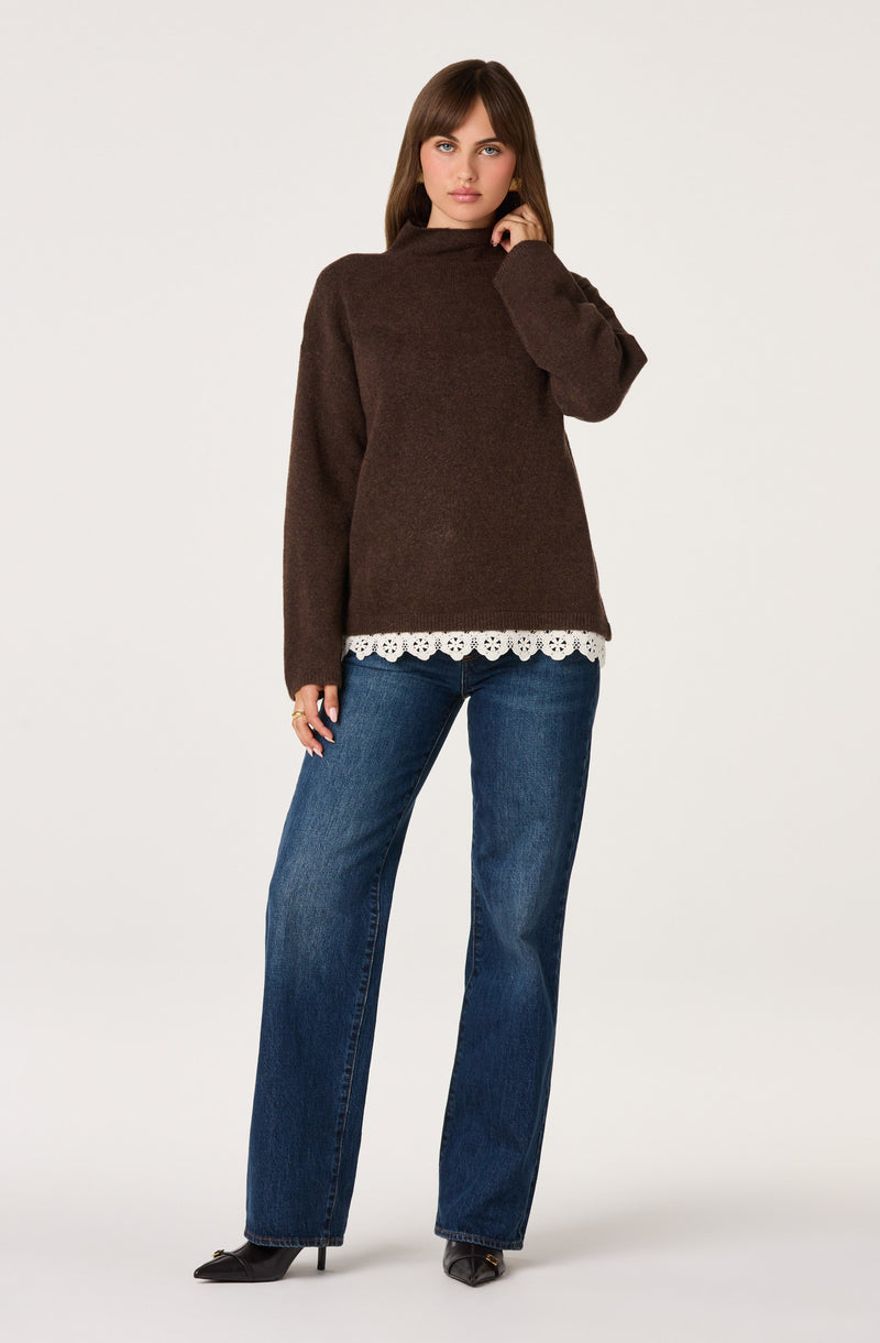 Woman wearing a brown sweater with lace hem and blue jeans.