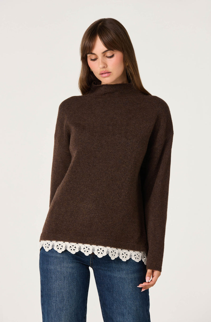 Woman wearing a brown sweater with a white lace-trimmed hem, paired with blue jeans.