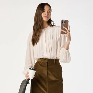 Woman wearing a cream blouse with pleats and long sleeves, paired with a brown skirt.