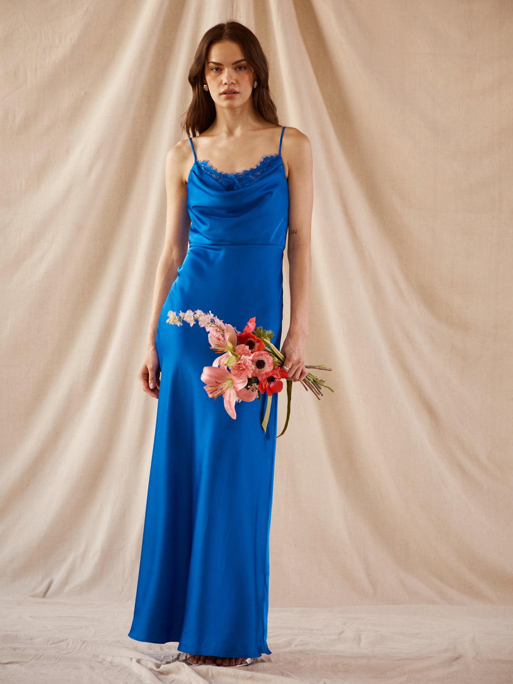 Woman in a bright blue slip dress with lace details, holding a pink flower bouquet.