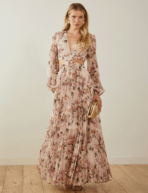 Woman in a long, floral, pink and beige dress with cut-outs at the waist, holding a gold clutch.