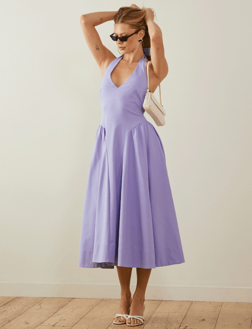 Woman in a lavender sleeveless midi dress, black sunglasses, white heels, and a small white purse.