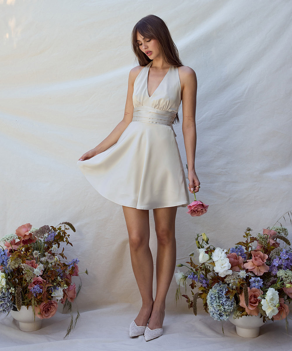 Woman in a white dress standing between two floral arrangements on a plain background