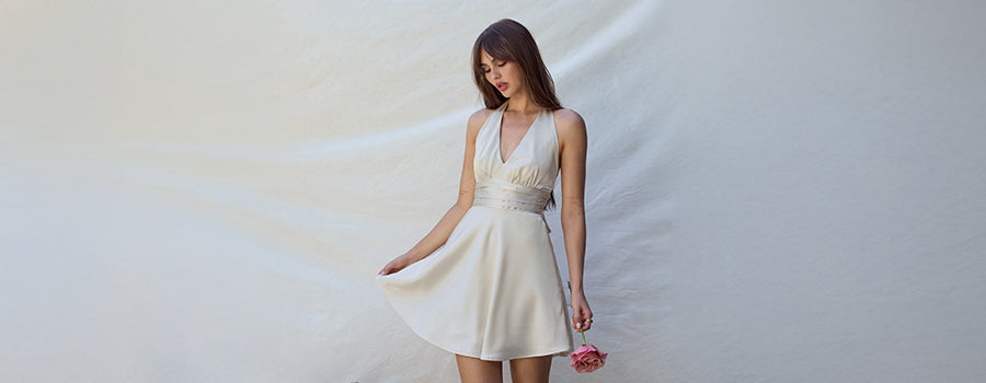 Woman in a white dress holding fabric against a plain background