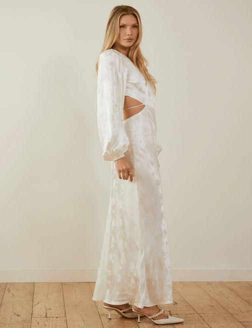 Woman in white satin dress with long sleeves, cut-out side, and pointed heels.