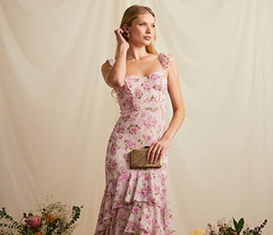 Woman in a long, floral pink and purple dress with ruffled hem, holding a clutch.