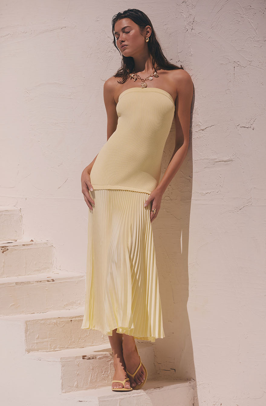 Woman in a strapless, ribbed yellow dress with a pleated skirt, wearing nude heels.