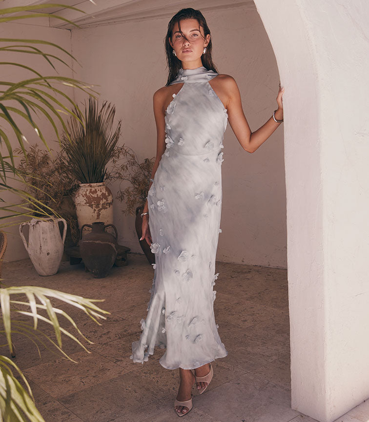 Woman wearing a sleeveless, high-neck, silver-grey satin dress with floral appliqué details.