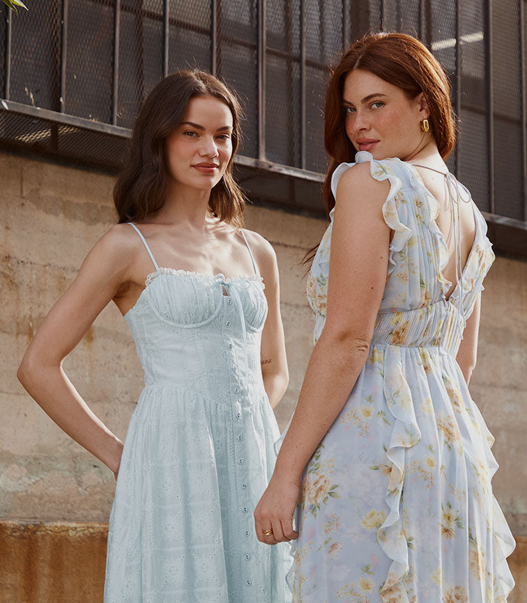 Two women in light-colored dresses, one with spaghetti straps and ruffles, the other with a floral print and ruffled sleeves.