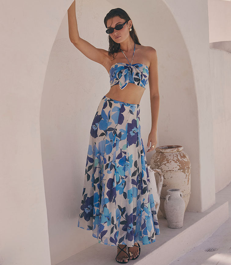 Woman in blue and white floral halter top and matching long flowy skirt, wearing sunglasses.