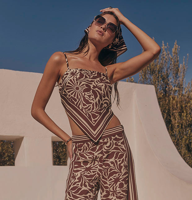 Woman wearing a brown and beige patterned sleeveless top and matching pants, accessorized with sunglasses and a headscarf.