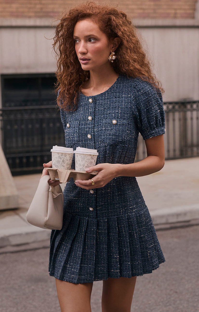 Woman wearing a navy blue textured dress with pearl buttons and a pleated skirt.