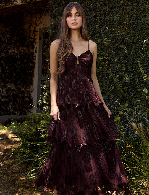 Woman wearing a dark red dress with floral patterns in an outdoor setting.