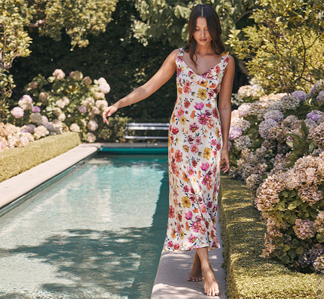 Woman in a floral dress standing by a pool with flowers and greenery around