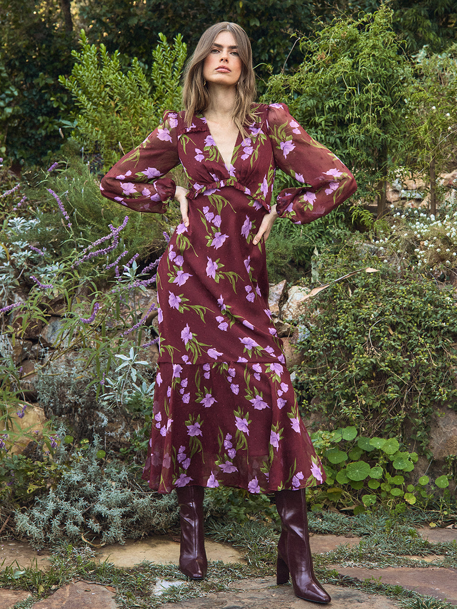 Woman in a burgundy floral dress standing in a garden