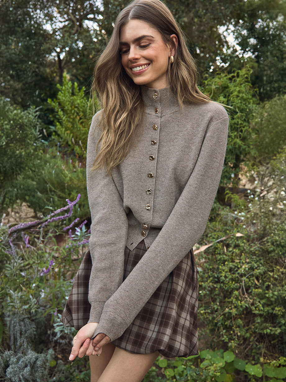 Woman wearing a gray cardigan over a plaid dress in a garden setting