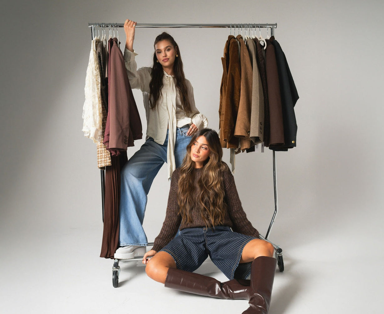 Two women with a rack of clothes on a plain background