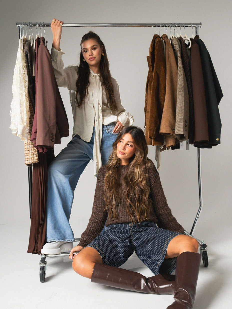 Two women with a rack of clothing in a neutral setting