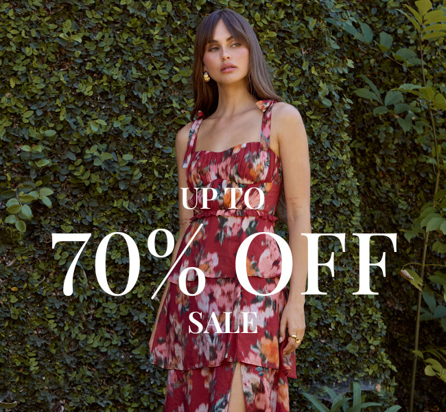 Woman in a sleeveless, floral dress with a layered skirt, standing outdoors in front of greenery.