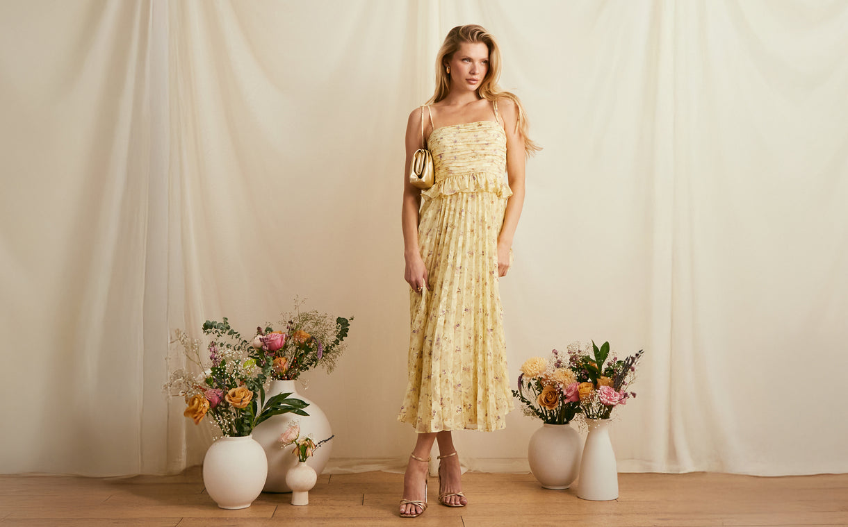 Woman in a yellow strapless dress with ruffles and floral patterns, holding a small gold purse.
