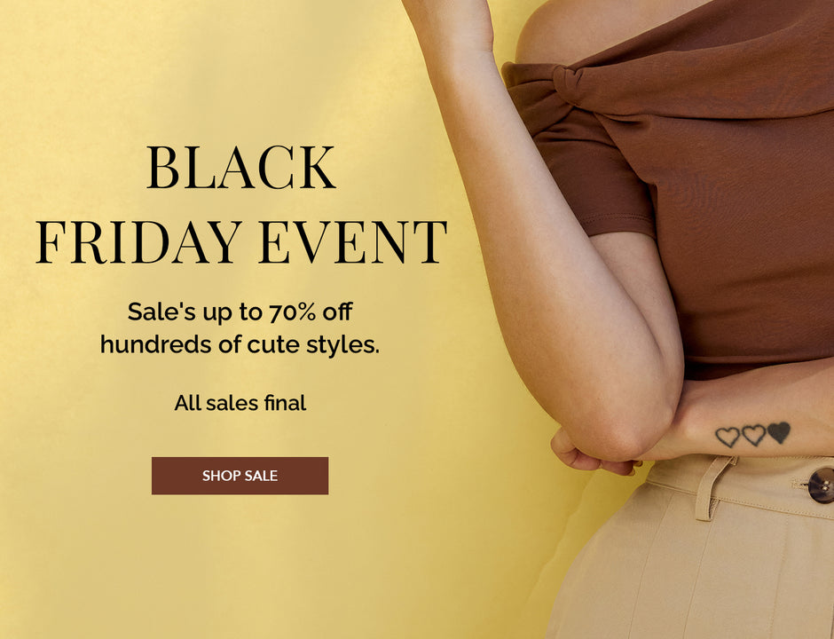 Person wearing a brown off-shoulder top and beige pants, with small heart tattoos on wrist.