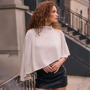 Woman in a beige cape-style top and a black leather skirt standing outdoors.