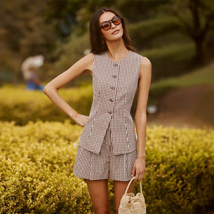 Woman wearing a sleeveless, checkered vest and matching shorts, holding a small woven bag.