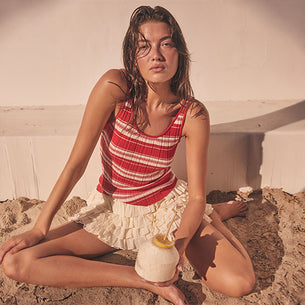 Woman wearing a red and white striped sleeveless top and a ruffled cream-colored skirt.
