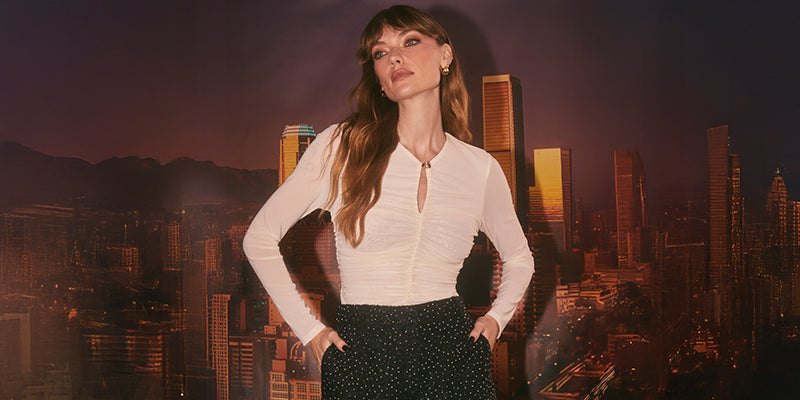 A woman is wearing a fitted white long-sleeve button-up blouse with a collar and a slight gathering detail in the front. She has paired it with high-waisted black pants that have a small, white polka dot pattern.