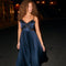 Woman in a dark blue, pleated evening dress with lace details on the bodice.