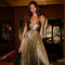 Woman wearing a gold, pleated, sleeveless dress with thin straps in a dimly lit room.