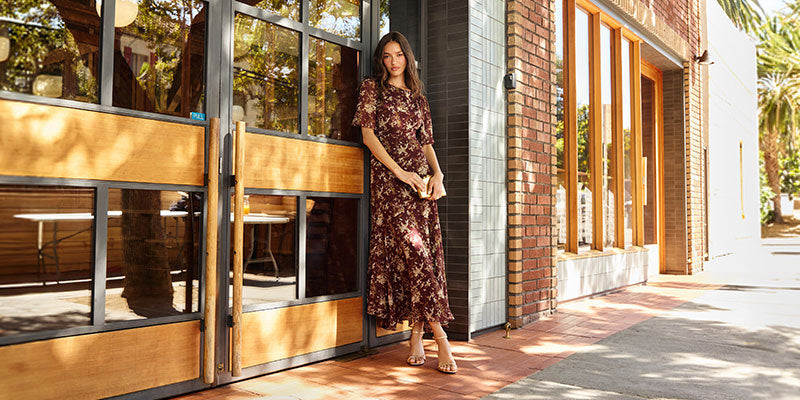 Woman in a long, floral-patterned dress standing outside a building.