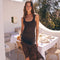 Young woman in a black ribbed tank top holding a sheer brown skirt outdoors, sunny day.