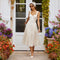 Woman in a white lace sleeveless midi dress, wearing sunglasses and a headscarf.