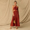 Woman in a red pleated halter dress with cutouts at the waist, holding a gold clutch.