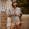 Woman in sunglasses wearing a beige checkered jacket, striped shirt, and beige shorts.