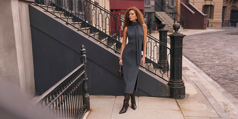 Woman in a sleeveless, high-neck, gray dress with side slits, and brown knee-high boots.