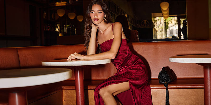Woman in a strapless, deep red, pleated gown sitting at a table inside a restaurant.