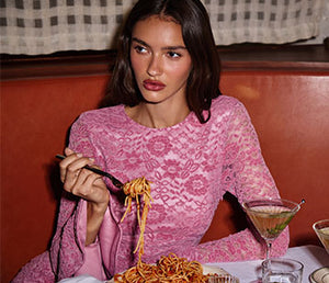 Woman in pink lace long-sleeve top eating spaghetti at a table.