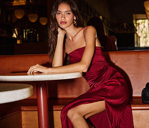 Woman in a strapless, deep red, ruched dress with a slit, seated at a table.