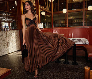 Woman in a black lace top and a long, pleated bronze skirt in a restaurant.