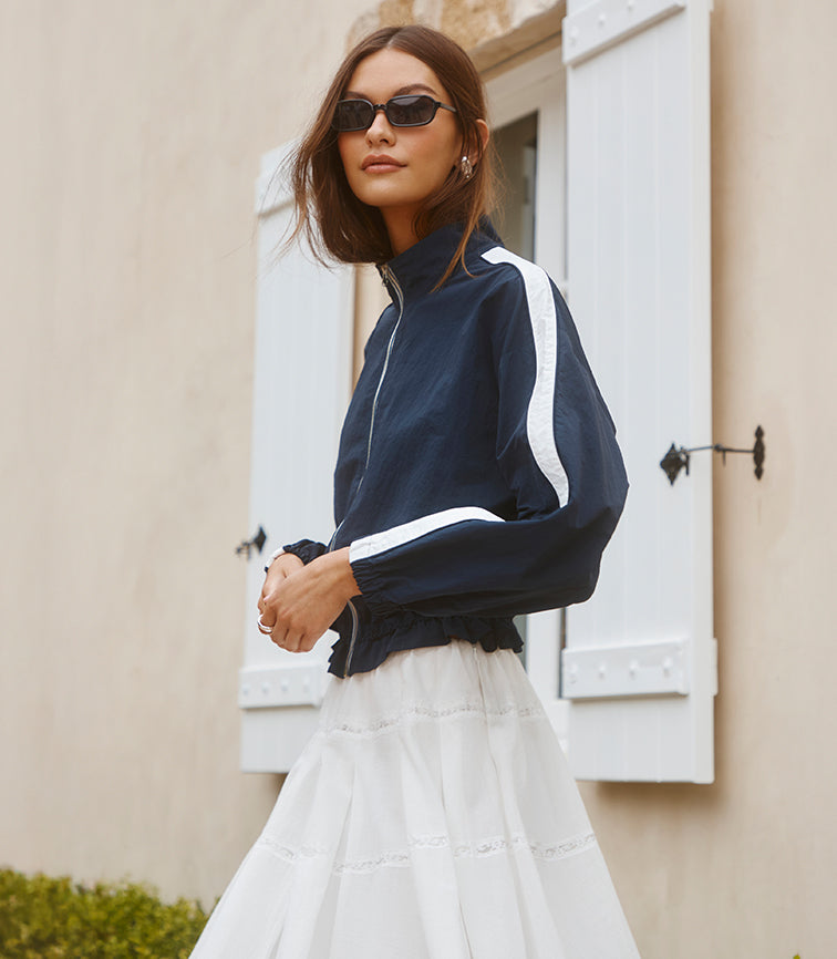 Woman wearing a navy blue jacket with white stripes and a white skirt.