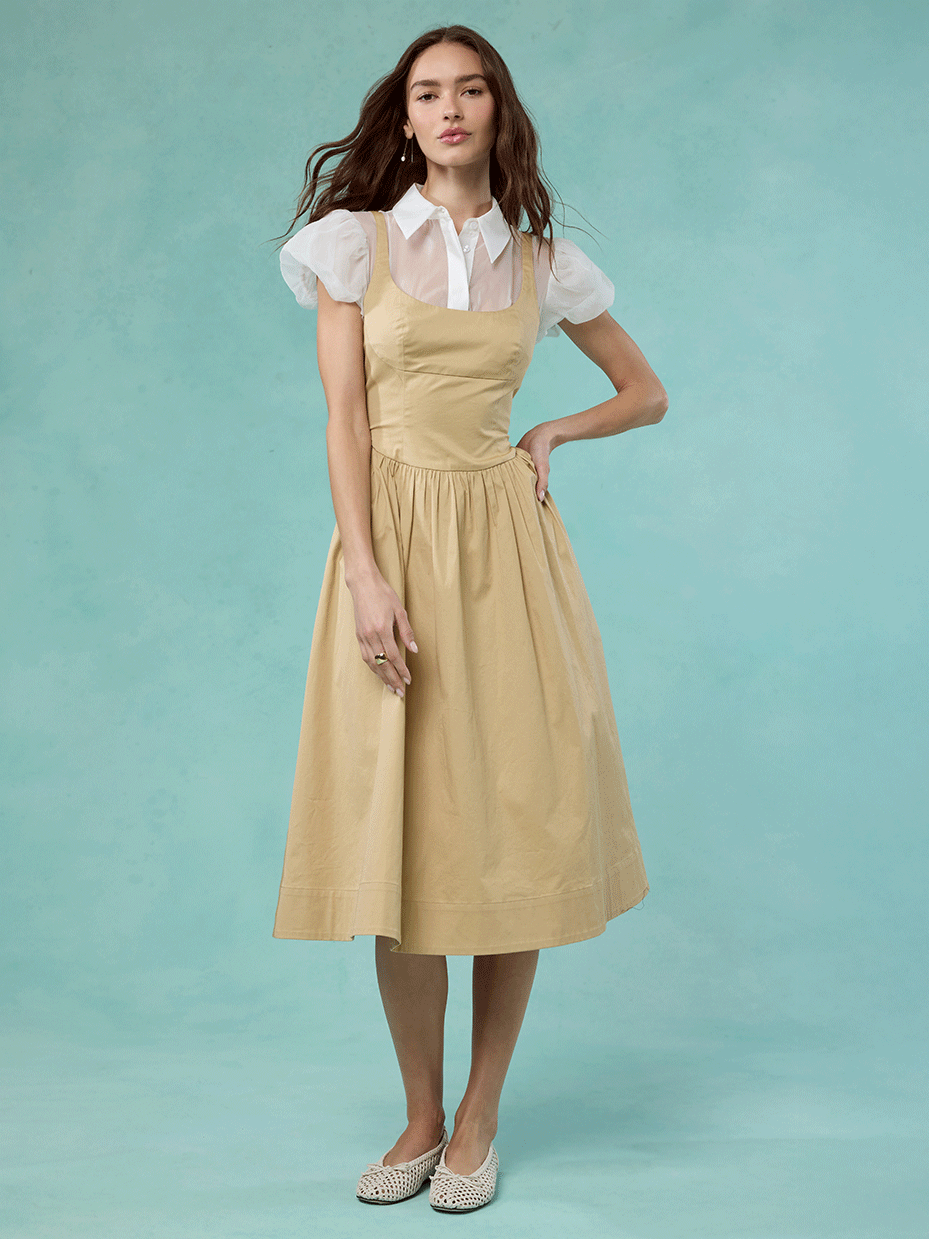 Woman wearing a white blouse with puffed sleeves and a beige pinafore dress.