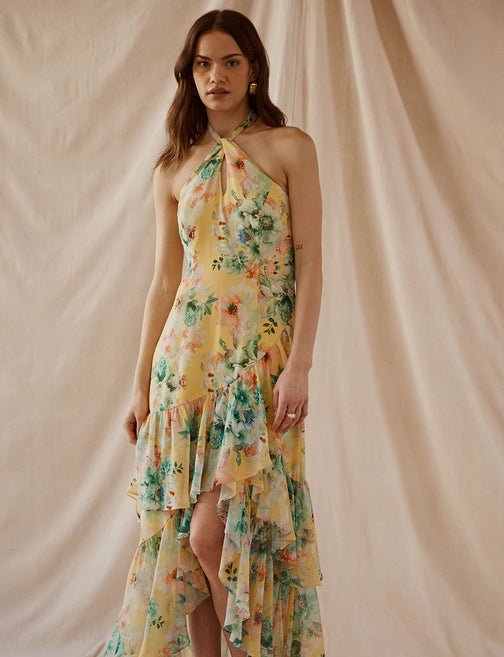 Woman wearing a long, yellow floral halter dress with ruffled hem and tiered layers.